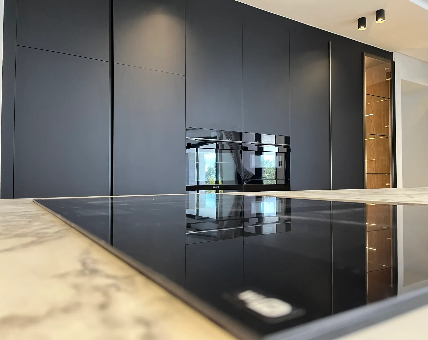 Matte black tall units with marble island and induction hob